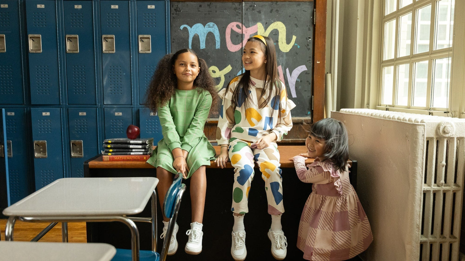 Girls sitting on a desk in front of a chalkboard at school