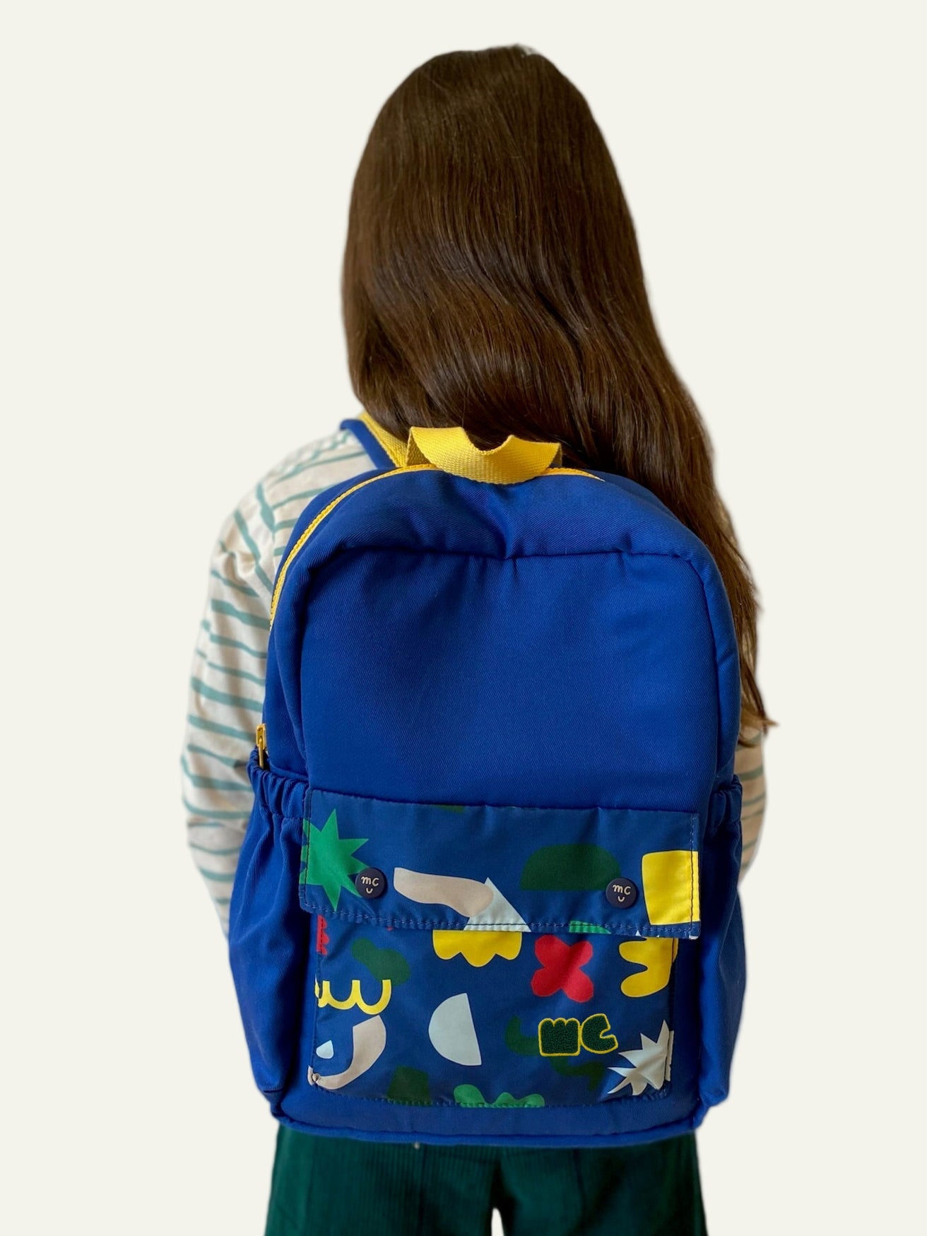 Person wearing a blue backpack with colorful designs on a plain background