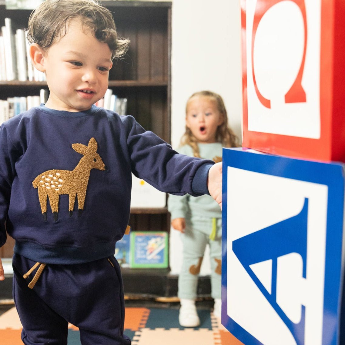 Child wearing a navy blue outfit with a deer design, interacting with a colorful sign in a classroom setting.