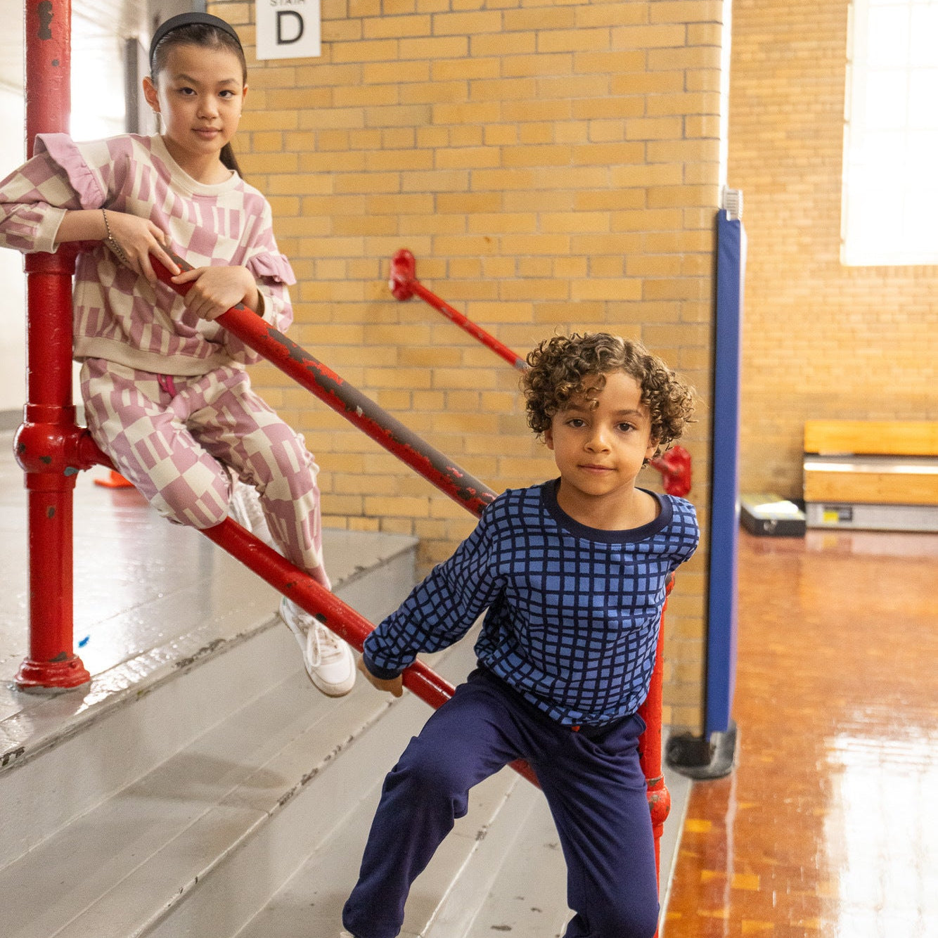 Two children playing on a playground structure with red and blue railings.