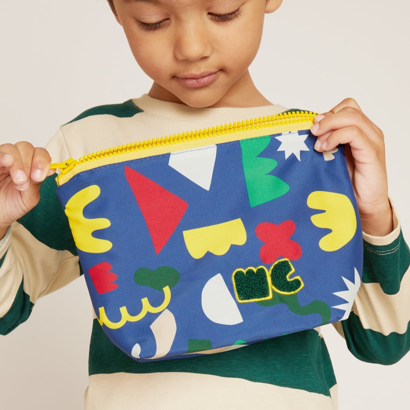 Child holding a colorful pouch with geometric patterns on a plain background